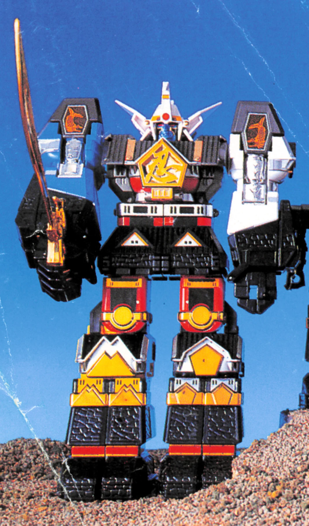 Bandai’s DX Muteki Shogun toy standing on a miniature rocky set, with a gold sword raised and all five robots combined.