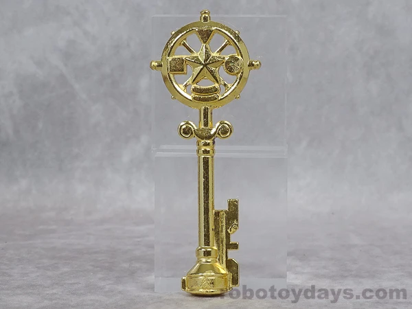 Gold-colored Legendary Key accessory with a circular bow and broad rectangular tip, resting on a clear photographic display stand.